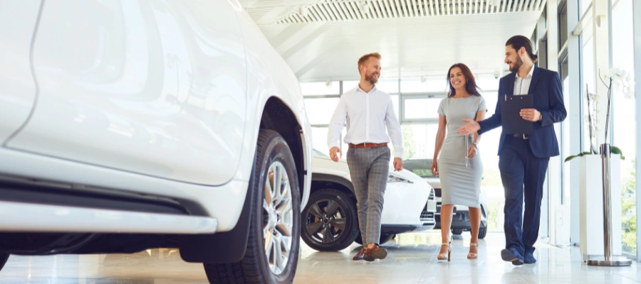 F&I managers walks with man and woman in car dealership showroom