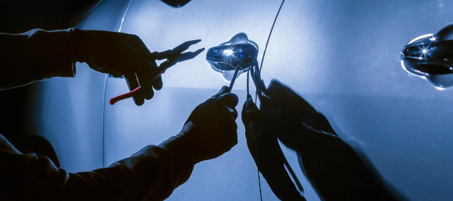 White car with shadowy arms at driver door handle holding tools attempting to break in.
