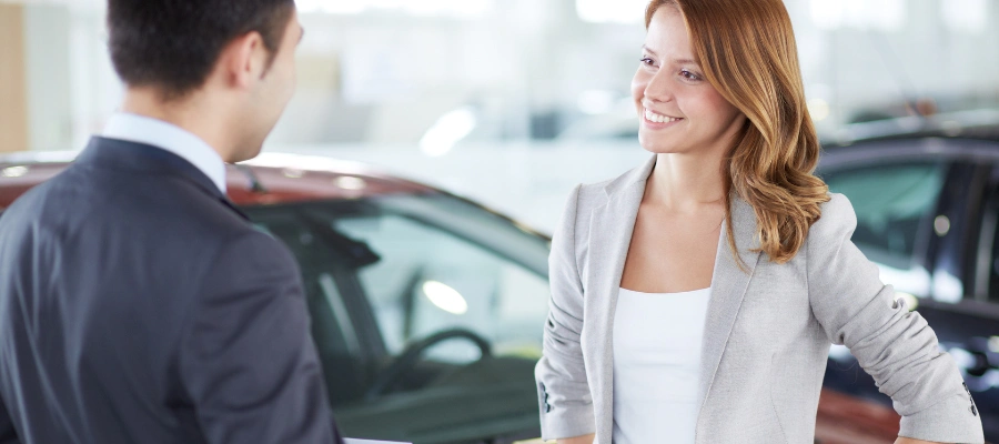 adult salesman talking to younger woman adult car buyer in car dealership